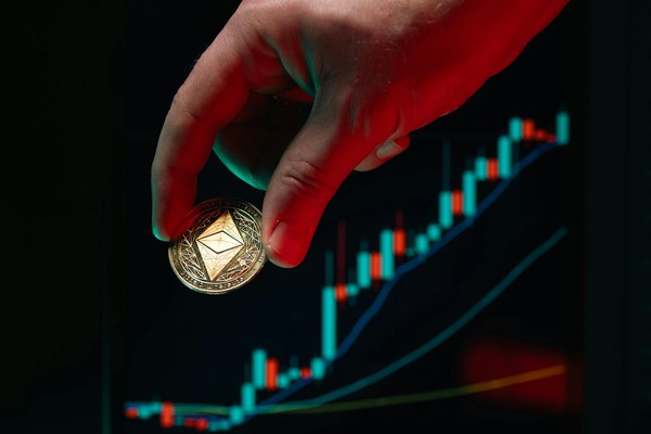 Hand holding an Ethereum coin in front of a rising cryptocurrency candlestick chart