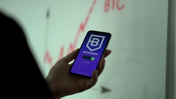 Smartphone showing a blockchain wallet app connecting, with a rising BTC chart in the background